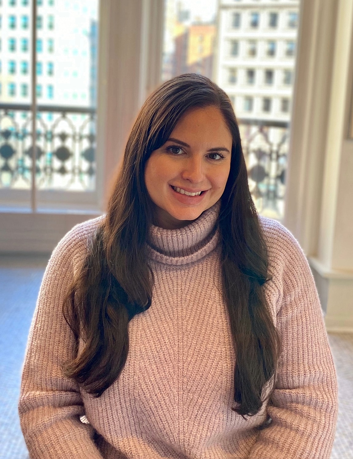 Smiling woman in cozy sweater by window.