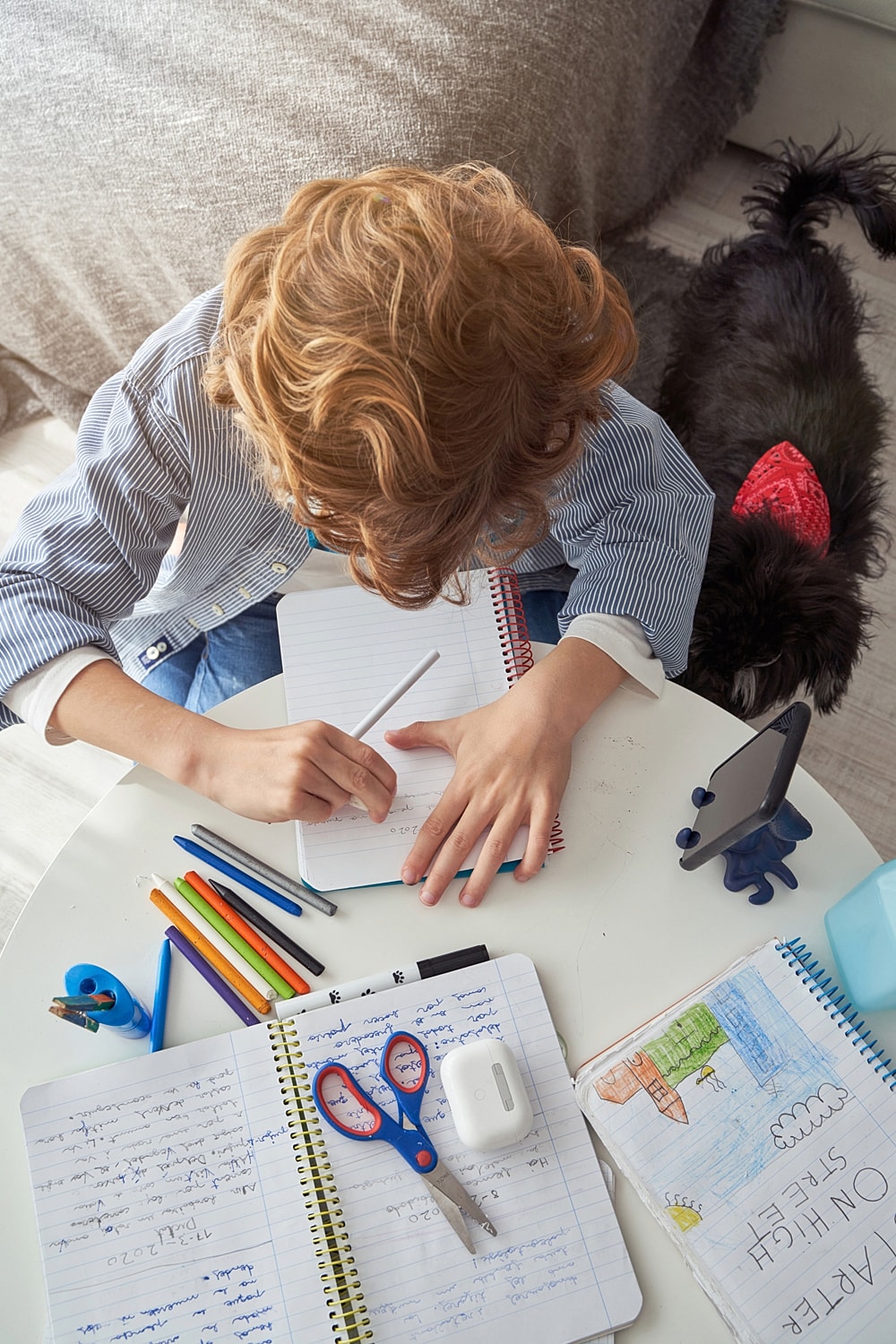 Child writing on notebook with colorful supplies.