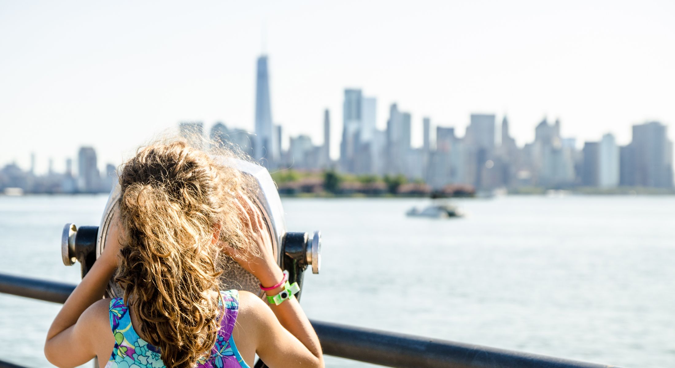 Child using binoculars with city skyline backdrop.