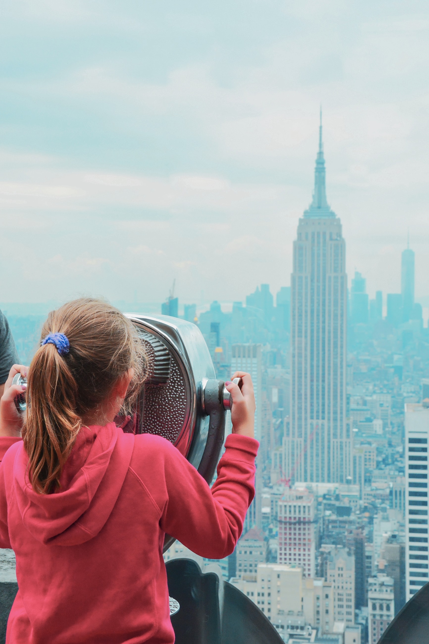 Child using binoculars overlooking city skyline.