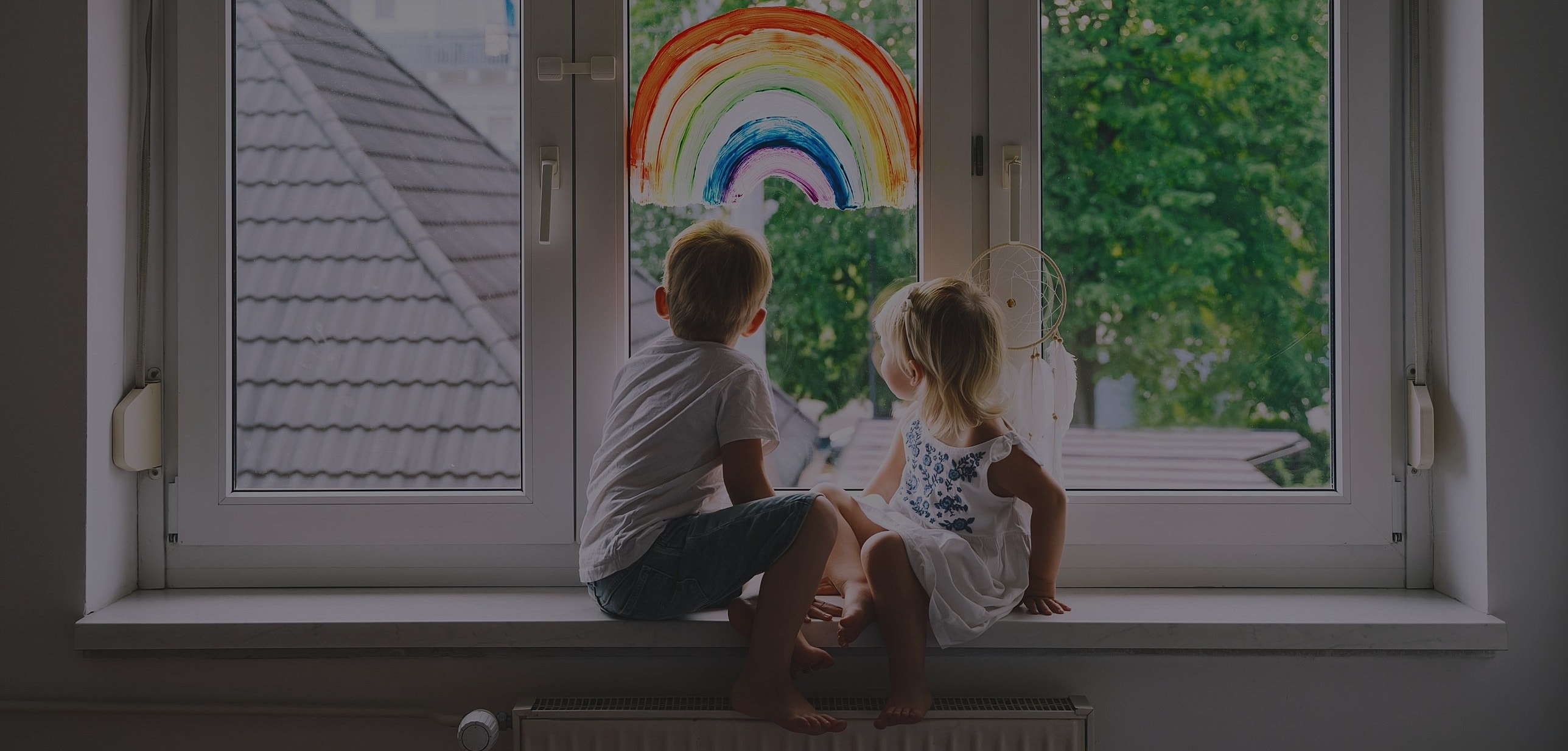 Children admiring a rainbow painting by window.