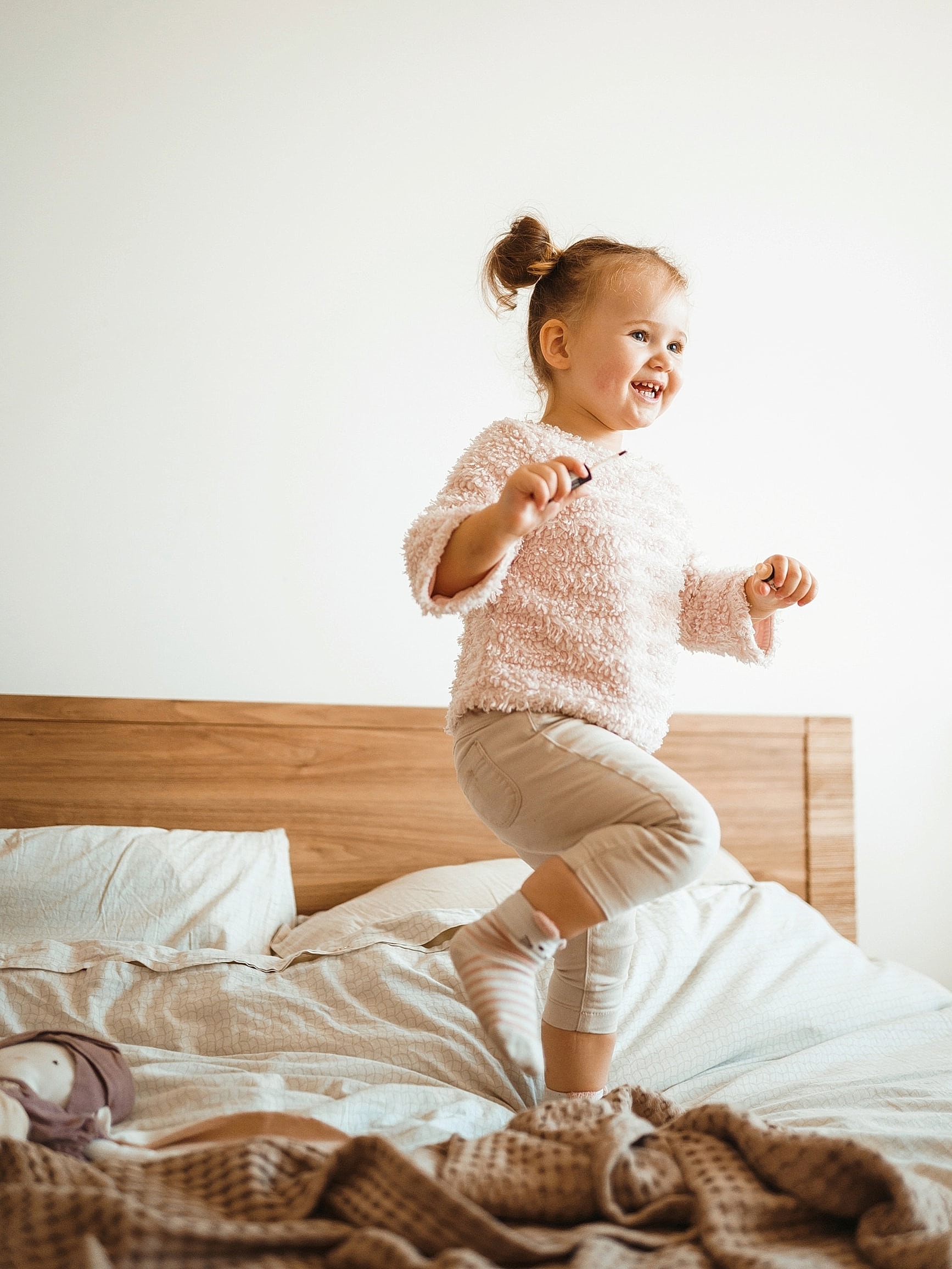 Child hopping on one foot joyfully on bed in cozy sweater.